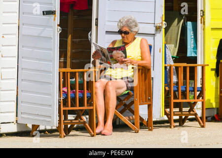 Lyme Regis, Dorset, Regno Unito. Il 13 agosto 2018. Regno Unito Meteo. Una donna leggendo una rivista in un lungomare beach hut alla stazione balneare di Lyme Regis in Dorset come lei gode del ritorno del caldo e soleggiato incantesimi dopo un weekend di cielo nuvoloso e pioggia. Credito Foto: Graham Hunt/Alamy Live News Foto Stock