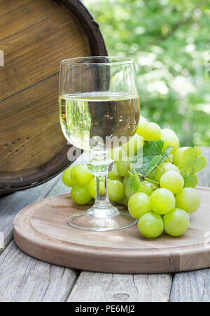 Un bicchiere di vino e uva verde su un tagliere di legno in un rustico oudoor impostazione Foto Stock