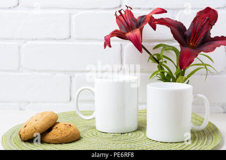 Due white tazza da caffè mockup con scuri giglio di borgogna e cookie. Boccale vuoto mock up per la promozione del design. Foto Stock