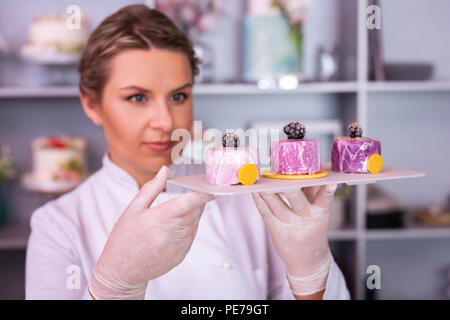 Blue-eyed chef femmina tenendo la piastra bianca con tre torte di frutta Foto Stock