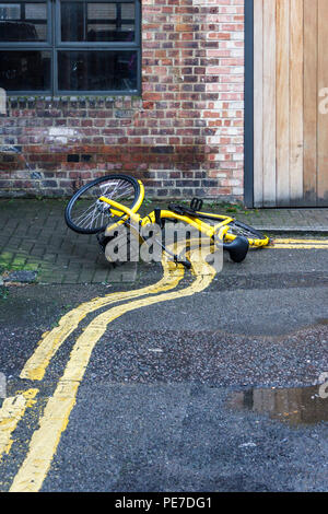 Un giallo Ofo bicicletta condivisa sventatamente abbandonato sul doppio giallo linee in un vicolo a Islington, London, Regno Unito Foto Stock