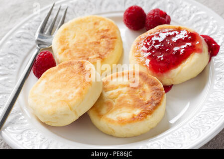 Cottage cheese frittelle o syrniki con confettura di lamponi sulla piastra bianca, vista ingrandita. Russo, Ucraino cucina. Una sana colazione gustosa Foto Stock