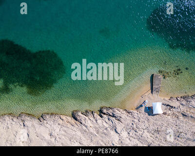 Vista aerea di una tenda alla moda, il coperchio dalla sun. Rocce sul mare e il mare trasparente pavimento. Relax e vacanze sotto una tenda bianca circondata da roccia Foto Stock