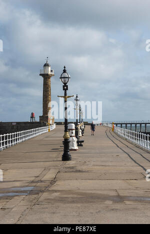 Il Molo di Ponente a Whitby sulla costa del North Yorkshire, Inghilterra. Un uomo cammina lungo su una soleggiata giornata di primavera. Foto Stock