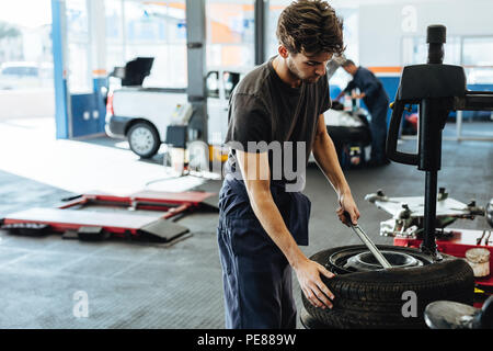 Repairman sostituzione pneumatico sulla ruota in officina. Cambio meccanico pneumatico auto in una stazione di servizio. Foto Stock