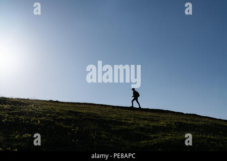 SIlhouette di una donna solitarie passeggiate al tramonto su una collina. Foto Stock