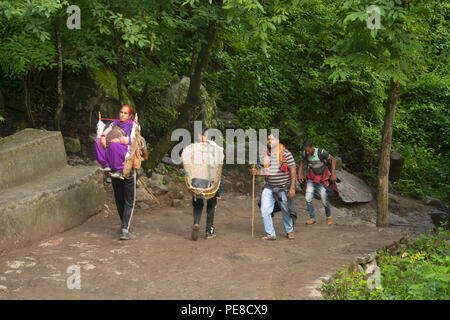 UTTARAKHAND, INDIA, giugno 2018, porter porta una vecchia donna fino alla montagna in un cesto di vimini Foto Stock