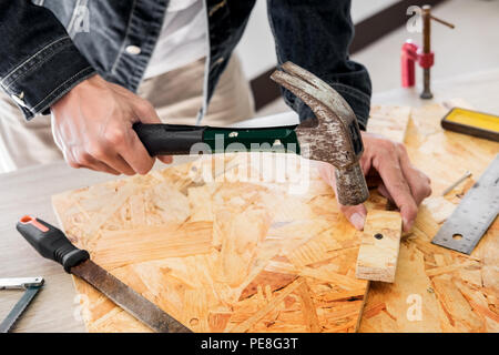 Carpenter operando con cautela guardando i piani di lavoro in falegnameria. Egli è imprenditore di successo al suo posto di lavoro. martellare un chiodo supporta sulla build Foto Stock
