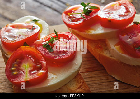 Bruschetta con pomodori ciliegia, mozzarella, basilico e baguette su uno sfondo di legno. Insalata caprese. Foto Stock