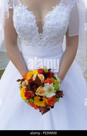 Giovane sposa caucasica indossando un lacy abito da sposa e tenendo un round e vibrante estate bouquet di fiori nella parte anteriore Foto Stock