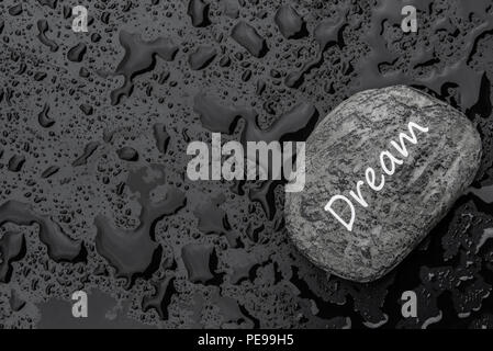 Immagine concettuale con la parola sogno scritto su una pietra, su uno sfondo nero cosparso di gocce di pioggia. Foto Stock
