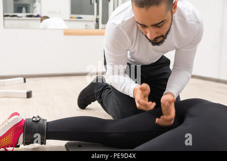 Maschio adulto trainer con camicia bianca womans massaggiante coscia in palestra con pavimento in legno e pareti di colore bianco Foto Stock