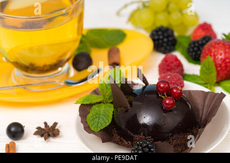 Gourmet cioccolato scuro bonbon con ribes rosso servito con una tazza di caldo speziato tè al limone e un assortimento di frutti di bosco freschi con la menta Foto Stock