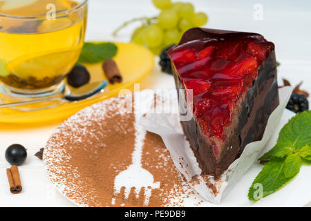 Gourmet torta al cioccolato guarnita con fragole servite su un piatto con il cacao in polvere e cospargere con sagoma a forcella a fianco di una tazza di acqua calda tè al limone Foto Stock