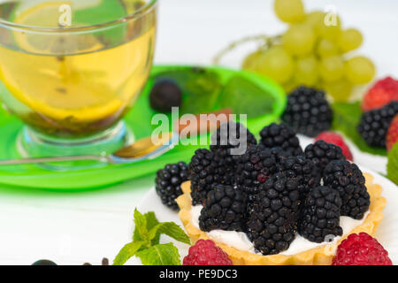 Blackberry fresco crostata con il piccante tè al limone in un bicchiere di vetro servita su un sfondo rosa in una vista ravvicinata Foto Stock