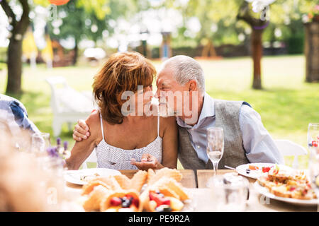 Coppia senior seduti al tavolo su un party in giardino, toccando nasi. Foto Stock