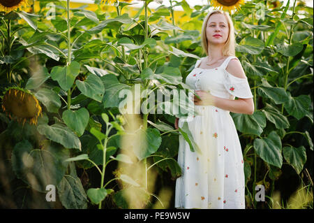 Bionda donna incinta nel campo di girasoli. Momenti felici di gravidanza. Foto Stock