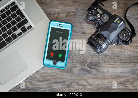Appartamento laico, tavolo in legno top con computer portatile, fotocamera retrò e smartphone con chiamante sconosciuto. Foto Stock