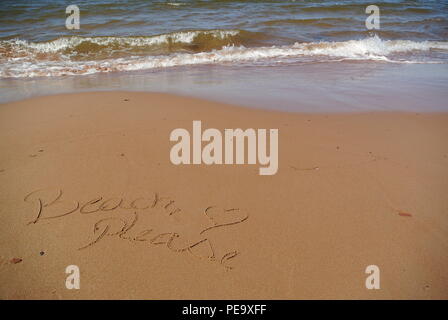 Le parole 'Beach si prega di' splendidamente manoscritta su la sabbia rossa su una spiaggia con il mare blu e un'onda nella parte superiore, Prince Edward Island, Canada Foto Stock