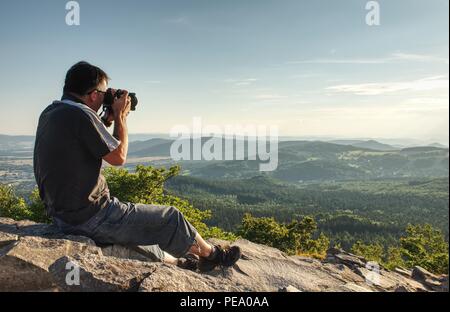 Fotografo di natura creare arte sul punto di vista nelle montagne. Uomo che guarda nel mirino del suo grande fotocamera, prendendo foto di borning giornata incredibile. Foto Stock