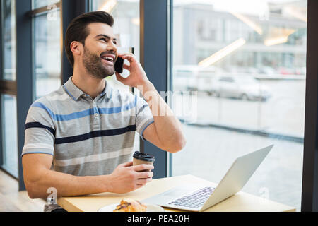 In una piacevole conversazione. Felice positivo Nizza uomo seduto nel caffè e ridere mentre avente una piacevole conversazione telefonica Foto Stock
