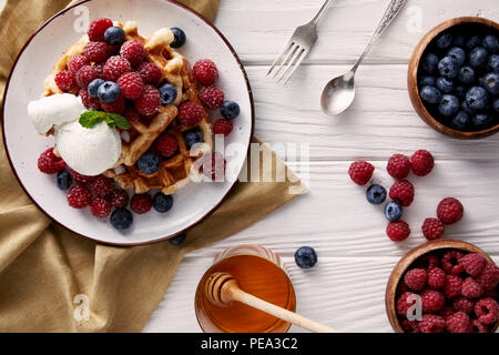 Appena cotto cialde belghe con il miele, gelati e bacche di colore bianco sul tavolo di legno Foto Stock