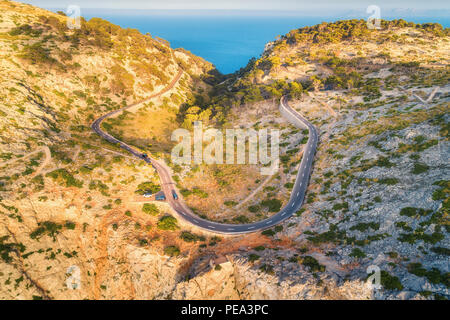 Vista aerea della curva di montagna strada con vetture, foresta verde al tramonto in estate in Europa. Paesaggio con strada asfaltata, alberi sulle rocce. Autostrada del thr Foto Stock