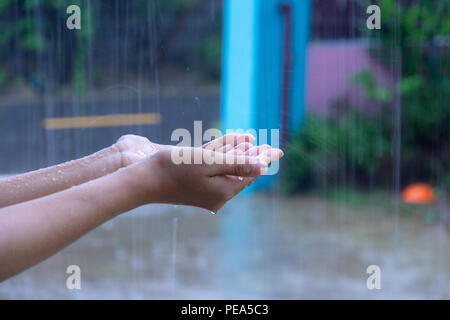 Close up della donna di mettere la mano sotto la pioggia la cattura di gocce di pioggia, il concetto di acqua. Foto Stock