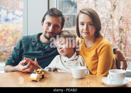 Ritratto di white Caucasian famiglia felice di tre madre, padre e figlio, seduti al ristorante cafe a tavola, sorridente giocando, autentico stile di vita Foto Stock