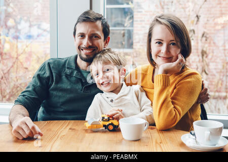 Ritratto di white Caucasian famiglia felice di tre madre, padre e figlio, seduti al ristorante cafe a tavola, sorridente giocando, autentico stile di vita Foto Stock