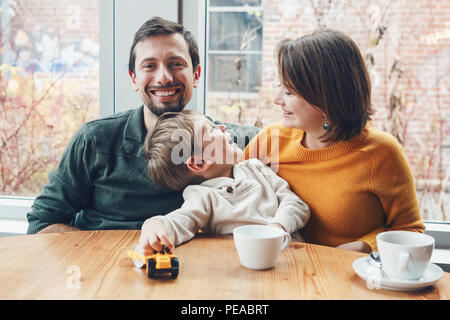 Ritratto di white Caucasian famiglia felice di tre madre, padre e figlio, seduti al ristorante cafe a tavola, sorridente giocando, autentico stile di vita Foto Stock