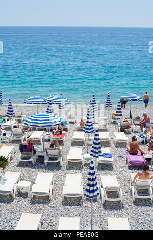 Nizza, Francia -26 maggio 2018- Vista di ombrelloni e sedie a sdraio con strisce blu e bianche sulla spiaggia di ghiaia sotto la Promenade des Anglais lungo t Foto Stock