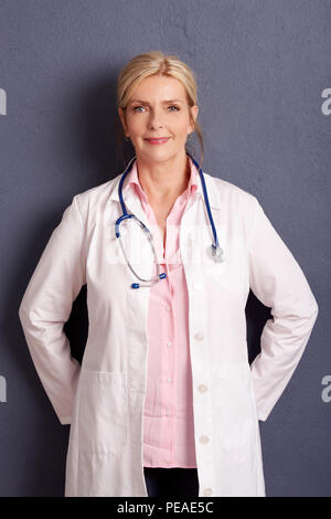 Ritratto di bella femmina matura medico permanente al muro grigio. Foto Stock