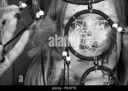 Foto in bianco e nero di una bella e giovane ragazza con un dream catcher. La bambina guarda attraverso di lui con occhi spalancati. Foto Stock