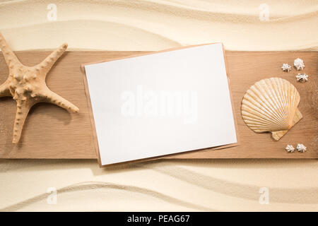 Lay piatto con carta bianca, stella di mare e conchiglie su tavola in legno sulla sabbia