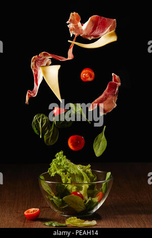 Ingredienti per insalata di verdure e prosciutto rientranti nel recipiente sopra un tavolo di legno Foto Stock
