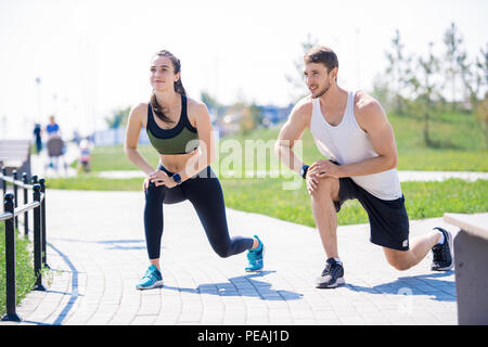 A piena lunghezza Ritratto di active coppia giovane facendo warm up esercizi durante il jogging insieme all'aperto nel parco, spazio di copia Foto Stock