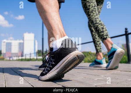 Sezione bassa colpo di piedi con le scarpe sportive di coppia giovane correndo insieme all'aperto alla luce diretta del sole, spazio di copia Foto Stock