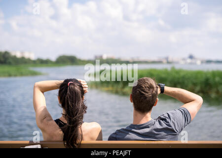 Sezione di alta vista posteriore della coppia giovane seduto su un banco di lavoro gode di vista lago nel parco, spazio di copia Foto Stock