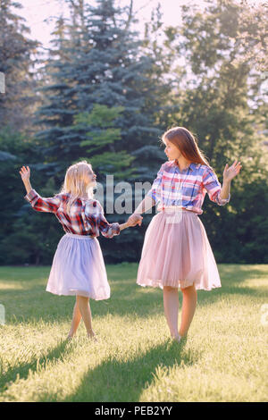 Ritratto di due sorridente divertenti ragazze caucasica sorelle in plaid shirt rosa e tulle tutu gonna, danza permanente a piedi nudi sull'erba nel parco forestale mead Foto Stock