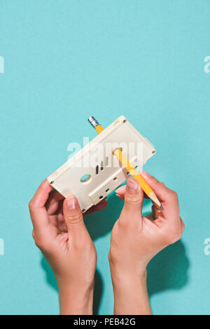 Vista parziale di donna holding white retrò di cassette audio e matita isolato su blu Foto Stock