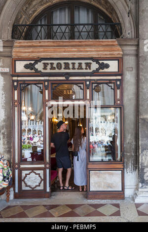 Coppia di turisti in piedi alle porte del caffè Florian, Piazza San Marco, San Marco, Venezia, Veneto, Italia, aperto nel 1720, è il caffè più antico d'Italia Foto Stock