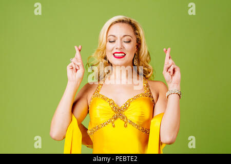 Dita incrociate, elegantemente vestito donna bionda in giallo abito da sera isolato sul verde di sfondo per studio Foto Stock