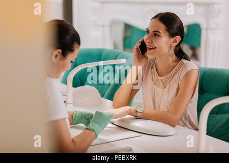 Occupato imprenditrice parla al telefono mentre avente manicure Foto Stock