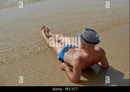Estate lifestyle ritratto di Giovani graziosi suntanned uomo in un cappello. Godersi la vita e seduto sulla spiaggia, il tempo di viaggio. Guardando il mare Foto Stock