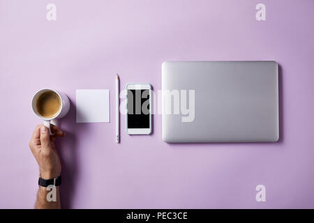 Ritagliato colpo di Uomo che piega tazza di caffè presso il luogo di lavoro con forniture sulla superficie rosa per mockup Foto Stock