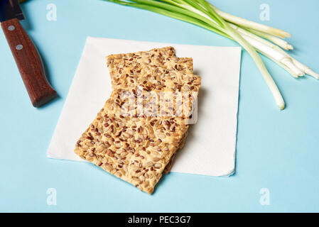 Vista ravvicinata del cookie con i semi, i porri e il coltello su sfondo blu Foto Stock