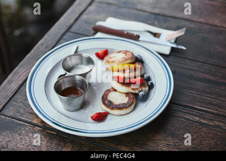 Close-up shot di gustoso formaggio frittelle con ciotole di immersioni e posate sul tavolo di legno Foto Stock