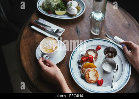 Ritagliato colpo di donna con formaggio frittelle e caffè sul tavolo di legno al ristorante Foto Stock