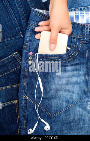 Femmina tenere la mano su di uno smartphone con le cuffie che si trova nella tasca anteriore dei jeans blu, full frame Foto Stock